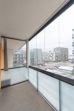 Camdan korkulukların ve kentsel konut binalarının manzaralı modern ev dairesi temiz minimalist estetiği vurguluyor.