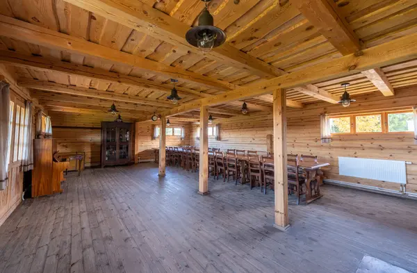 Uzun masalar, sandalyeler, konforlu bir şömine ve yan pencerelerden gelen doğal ışıklandırmanın yer aldığı taşralı ahşap yemek alanı, toplantılar veya halk yemekleri için sıcak ve davetkar bir ortam yaratıyor..