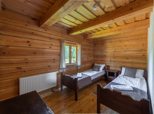 Sıcak ve davetkar, ahşap duvarlar, ikiz yataklar ve bir pencereden yansıyan doğal ışıklandırmayla rahat ve huzurlu bir atmosfer sağlayan kırsal bir yatak odası.