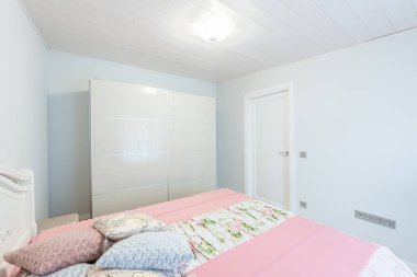 Zarif ve huzurlu bir yatak odası. Pastel tonlu yatak örtüsü, beyaz yatak başlığı ve minimalist modern gardırobu var. Basitliği ve rahatlama için rahat bir atmosferi vurguluyor..