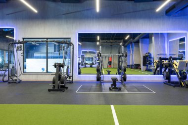 A spacious and modern gym facility featuring state-of-the-art exercise machines and weights. The gym includes mirrored walls and green turf flooring, creating a vibrant and motivational environment.