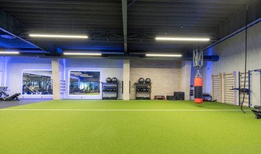 Spacious and modern workout facility featuring training equipment, a boxing bag, and vibrant artificial turf. Ideal for fitness enthusiasts or gym-related activities in a well-lit atmosphere.