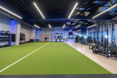 Spacious and modern gym featuring various exercise machines, a dedicated turf track area, and a clean, professional atmosphere for fitness enthusiasts to engage in strength training