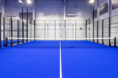Işıl ışıl mavi zeminli ve kort çizgileri, iyi ışıklandırılmış ve etrafını çevreleyen çevreleyen ve net olan boş bir kürek tenis kortu..