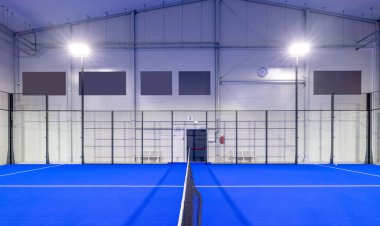 Işıl ışıl bir spor tesisi içinde, etrafı tel örgülerle çevrili, canlı mavi döşemeli, geniş raket tenis kortu. En uygun oyun deneyimi için özenle tasarlanmış