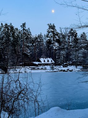 Winter landscape of a snowy pine forest, a wooden house and a frozen lake. High quality photo