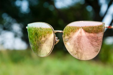 Yol ve arazinin yansıması olan güneş gözlükleri. Yaz tatili dışarıda. Yaz yansıtıcı gözlük ya da ayna gözlüğü. şık moda aksesuarlarının seçici odağı.