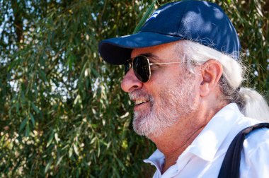 İspanyol asıllı, mutlu, yaşlı, şık, gri sakallı, yaz tarzı Küba şapkalı ve güneş gözlüklü bir adam..