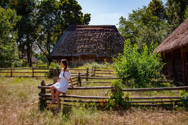 stock image Woman in summer farm. Authentic Ukrainian architecture. Woman outdoor. Ukrainian woman in summer village. Ukraine folk authentic house. Thatched house in Ukrainian village. Rustic wooden fences.