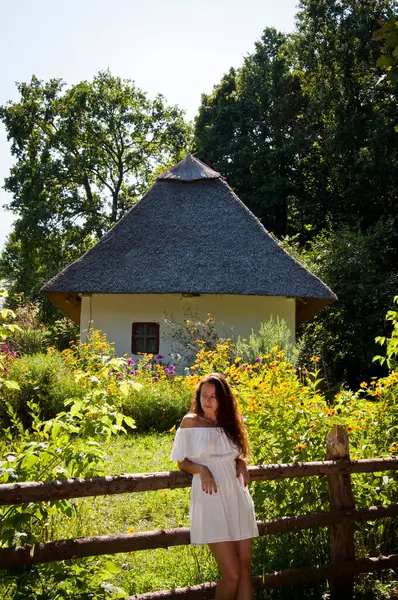 Ukrainian woman in summer village cottage. Ukraine folk authentic house. Thatched house in Ukrainian village. Woman in summer farm. Authentic Ukrainian architecture. Woman ethnographic outdoor.