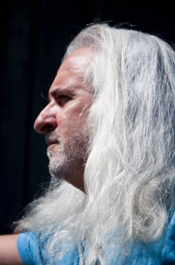 Latin kökenli olgun, karizmatik bir adam. Tıraşsız bir yüzü ve kır saçlı, açık hava profilinde uzun, sağlıklı bir saçı var..