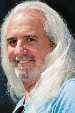 Latin kökenli, olgun, mutlu, tıraşsız yüzlü, kır manzaralı, uzun, sağlıklı saçları olan bir adam..