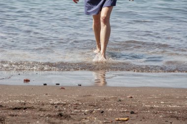 Deniz sahilinde yalınayak yürümek. Yaz tatili. Cilt bakımı. Uzay afişini kopyala. Gün batımında sahilde çıplak ayakla yürürken dalga kenarları köpürüyor..