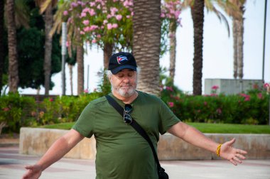 İspanyol kıdemli turist. Kıdemli turist palmiye ağacı sokağında yürüyor. Yaz tatili turisti. Yaşlı adam turistik caddede yürüyor. Seyahat güzergahı. Palmiye ağacı. İspanyol adam. Park ve açık hava.