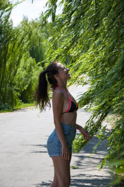 Yazın rüzgarda söğüt ağacı dalları arasında bir kadın. Yeşil rüzgarlı söğütlü kadın. Yaz kırsalında. Doğada açık hava yaşam tarzı. Söğüt ağacı rüzgarda dallanır. Hafif bir esinti.