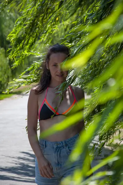 Yazın rüzgarda söğüt ağacı dalları arasında kırsal yolda yürüyen bir kadın. Kırsal yolda yürüyen bir kadın. Yaz kırsal gezintisi. Doğada açık hava yaşam tarzı. Rüzgarda söğüt ağacı dalları.