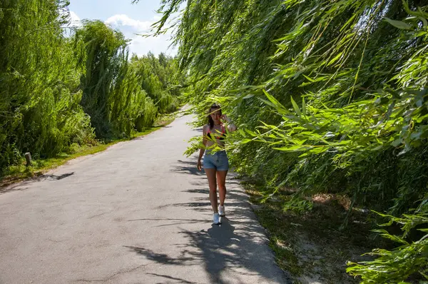 Yaz kırsal gezintisi. Açık hava yaşam tarzı. Rüzgarda söğüt ağacı dalları. Yazın rüzgarda söğüt ağacı dalları arasında kırsal yolda yürüyen bir kadın. Kırsal yolda yürüyen bir kadın. Yeşil manzara.