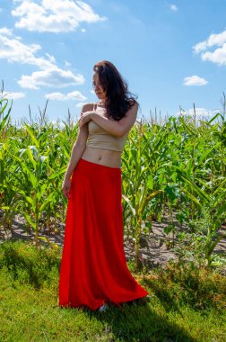 Doğa kaçışı. Yaz modası. Canlı kırmızı etekli İspanyol kız. Kırsal yaşam tarzı. Genç kız, renk farkı. Kadınsı güç ve güzellik, feminizm. Mısır tarlasında mavi gökyüzünün altında genç bir kadın. Cilt bakımı.
