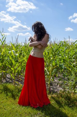 Mavi gökyüzünün altında tarlada genç bir kadın. Doğa kaçışı. Yaz modası. Canlı kırmızı etekli İspanyol kız. Kırsal yaşam tarzı. Genç kız, renk farkı. Kadınsı güç ve güzellik, feminizm..