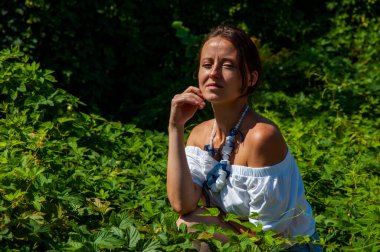 Bitkisel ilaçlar. Rahatlama inzivası. İnci kolyeli genç İspanyol kız, yeşil beyaz. Doğa terapisi. Yeşillik ormanında oturan bir kadın. Egzotik orman. Tropik güzellik. Sağlıklı cilt.