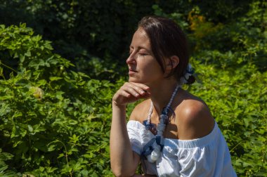 Rahatlama inzivası. İnci kolyeli genç İspanyol kız, yeşil beyaz. Doğa terapisi. Yeşillik ormanında oturan bir kadın. Egzotik orman. Tropik güzellik. Bitkisel ilaçlar. Güneşin tadını çıkarıyorum.