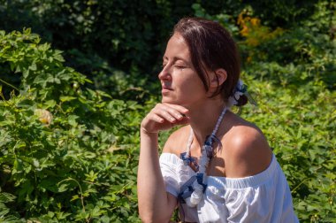 Yalnızlık ve özgürlük. Rahatlama geri çekilme yaşam tarzı. Düşünceli İspanyol kız, yeşil beyaz. Doğa kaçışı. Yeşillik ormanında oturan bir kadın. Boho yaz modası. Çarpıcı tropikal güzellik.