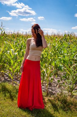 Canlı kırmızı etekli İspanyol kız. Kırsal yaşam tarzı. Genç kız, renk farkı. Kadınsı güç ve güzellik, feminizm. Mısır tarlasında mavi gökyüzünün altında genç bir kadın. Doğa kaçışı. Yaz modası.
