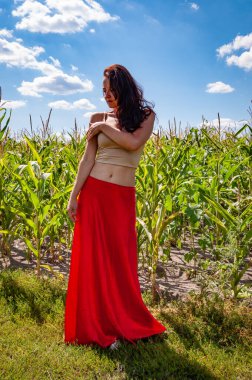 Genç kız, renk farkı. Kadınsı güç ve güzellik, feminizm. Mısır tarlasında mavi gökyüzünün altında genç bir kadın. Doğa kaçışı. Yaz modası. Canlı kırmızı etekli İspanyol kız. Kırsal yaşam tarzı. Güneş yanığı.