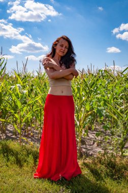 Doğa kaçışı. Yaz modası. Canlı kırmızı etekli İspanyol kız. Kırsal yaşam tarzı. Genç kız, renk farkı. Kadınsı güç ve güzellik, feminizm. Mısır tarlasında mavi gökyüzünün altında genç bir kadın, güneş ışığı....