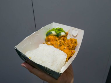 Beyaz kağıt bir kabın içine peynirli mayonez serpiştirilmiş tavuk pirinci.