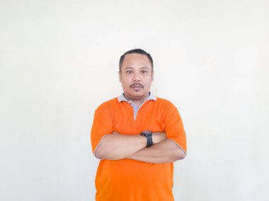 Turuncu tişörtlü Asyalı yetişkin erkek beyaz arka planda hareketler ve yüz ifadeleri yapıyor.