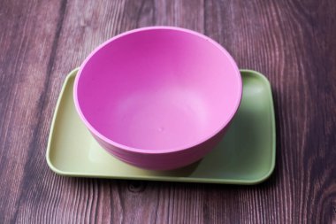 Plastikten yapılmış yiyecek kapları arasında kaseler, tabaklar ve tahta üzerinde pembe ve yeşil tabaklar yer alıyor.