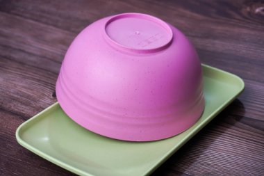 Plastikten yapılmış yiyecek kapları arasında kaseler, tabaklar ve tahta üzerinde pembe ve yeşil tabaklar yer alıyor.