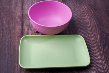 Plastikten yapılmış yiyecek kapları arasında kaseler, tabaklar ve tahta üzerinde pembe ve yeşil tabaklar yer alıyor.