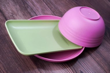 Plastikten yapılmış yiyecek kapları arasında kaseler, tabaklar ve tahta üzerinde pembe ve yeşil tabaklar yer alıyor.