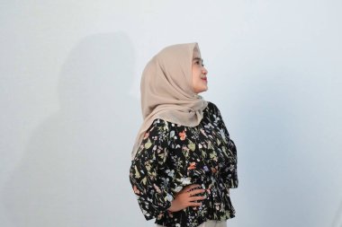 Asyalı Endonezyalı bir kadının tesettürlü, çiçekli siyah bir elbise giymesinin mutlu ifadesi.