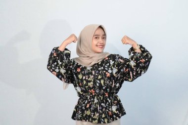 Asyalı Endonezyalı bir kadının tesettürlü, çiçekli siyah bir elbise giymesinin mutlu ifadesi.