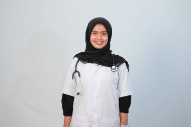 Doktor ve tıbbi konsept. Endonezyalı tesettürlü kadın doktor mavi ve beyaz arka planda tıbbi aktivite ifadesi yapıyor..