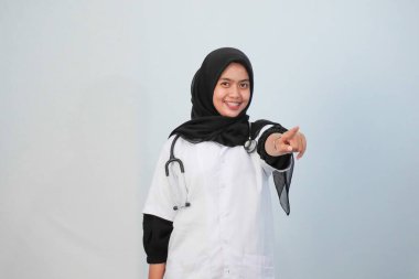 Doktor ve tıbbi konsept. Endonezyalı tesettürlü kadın doktor mavi ve beyaz arka planda tıbbi aktivite ifadesi yapıyor..