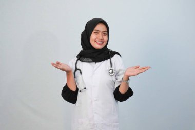 Doktor ve tıbbi konsept. Endonezyalı tesettürlü kadın doktor mavi ve beyaz arka planda tıbbi aktivite ifadesi yapıyor..