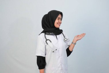 Doktor ve tıbbi konsept. Endonezyalı tesettürlü kadın doktor mavi ve beyaz arka planda tıbbi aktivite ifadesi yapıyor..