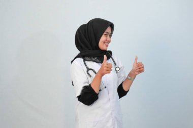 Doktor ve tıbbi konsept. Endonezyalı tesettürlü kadın doktor mavi ve beyaz arka planda tıbbi aktivite ifadesi yapıyor..