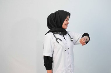 Doktor ve tıbbi konsept. Endonezyalı tesettürlü kadın doktor mavi ve beyaz arka planda tıbbi aktivite ifadesi yapıyor..