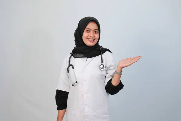 Doktor ve tıbbi konsept. Endonezyalı tesettürlü kadın doktor mavi ve beyaz arka planda tıbbi aktivite ifadesi yapıyor..