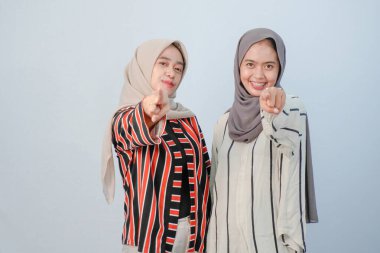 İki Asyalı Endonezyalı tesettürlü kadının, kahverengi ve beyaz çizgili giysiler içindeki mutlu ifadeleri.