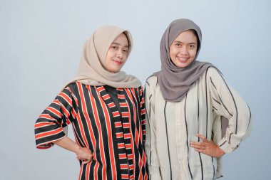 İki Asyalı Endonezyalı tesettürlü kadının, kahverengi ve beyaz çizgili giysiler içindeki mutlu ifadeleri.