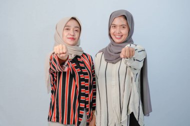 İki Asyalı Endonezyalı tesettürlü kadının, kahverengi ve beyaz çizgili giysiler içindeki mutlu ifadeleri.