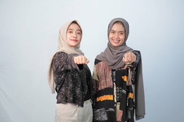 Siyah ve kahverengi desenli giyinen iki Endonezyalı kadın mavi-beyaz arka planda diğer renklerle birleştirilmiş.