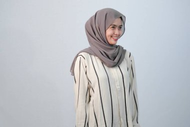 Endonezyalı Asyalı kadının bedeni tesettüre bürünmüş beyaz elbiseler ve çizgili motifler giyiyor.