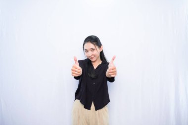 Siyah elbiseli Asyalı kadın beyaz arka planda başparmak işareti gösteriyor.